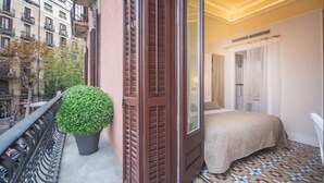 A balcony with a potted plant, a bed with a beige cover, and a patterned floor. - Anakena House (Barcelona)