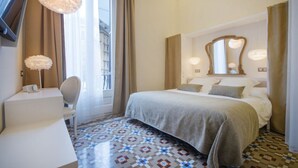 A hotel room with a bed, a desk, a chair, a large mirror, and a patterned floor. - Anakena House (Barcelona)