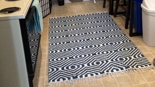 Une cuisine équipée d’une cuisinière, d’un évier, d’une table à manger avec des chaises, d’un tapis à motifs et d’une plante en pot.