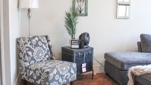 Un salon avec un fauteuil à motifs, un canapé gris, une petite table sur laquelle est posée une plante, une lampe et un miroir décoratif.