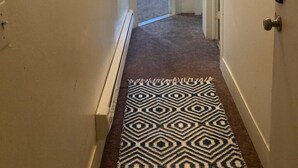 Un couloir avec un tapis à motifs, une porte dotée d’un miroir et un mur orné d’objets décoratifs.