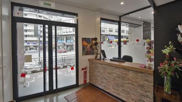 A reception area with a glass door, a fire extinguisher, a desk with a computer, and a vase with flowers. - Hotel Mino (Ourense)
