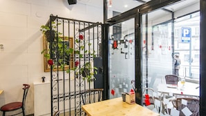 A modern indoor dining area with a wooden table and four chairs, a decorative metal partition with plants, and a view through large glass windows. - Hotel Mino (Ourense)