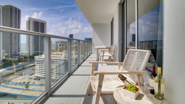 Un balcon avec vue sur la ville, des meubles en bois et une bouteille de vin.