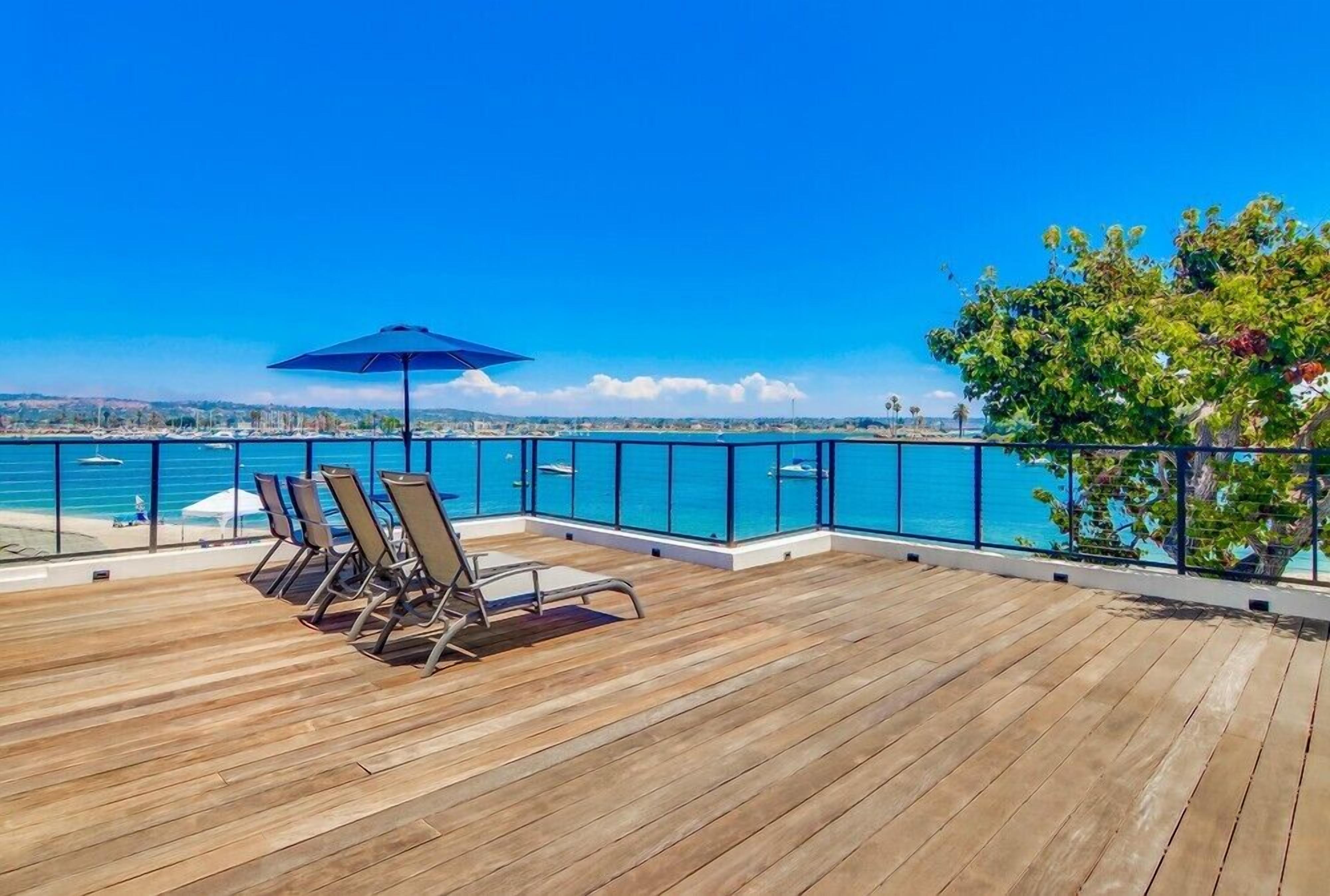 Une terrasse en bois avec des chaises longues et un parasol, donnant sur une mer d’un bleu limpide.