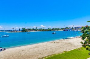 A beach with boats, clear blue water, and a distant building.