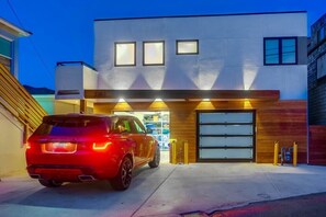 Uma casa moderna de dois andares com garagem, um carro vermelho estacionado na frente e uma entrada bem iluminada.