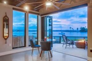 Quarto moderno com grandes janelas, uma mesa de vidro redonda, duas cadeiras e uma lareira.
