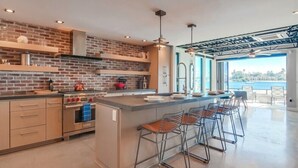A modern kitchen with a brick backsplash, stainless steel appliances, and a large island with bar stools. - Modern WaterFront House * 2 Levels * 4 Parking * AC (San Diego)