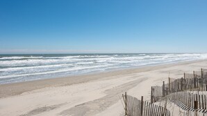 Ein Strand mit einer Holzzahlung im Vordergrund und Wellen, die auf das Ufer treffen.