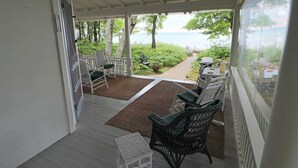 A covered porch with outdoor seating, a view of the sea, and a pathway leading to a barbecue area. - Historic cottage just minutes from downtown Harbor Springs! (Harbor Springs)