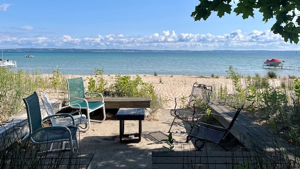 A beachside seating area with chairs and a table, overlooking a calm sea with boats in the distance. - Historic cottage just minutes from downtown Harbor Springs! (Harbor Springs)