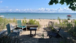 A beachside seating area with chairs and a table, overlooking a calm sea with boats in the distance. - Historic cottage just minutes from downtown Harbor Springs! (Harbor Springs)