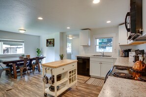 A modern kitchen with wooden flooring, white cabinetry, a built-in stove, and a dining area with a wooden table and chairs. - Adorable Coeur d'Alene Home < 2 Mi to Lake! (Coeur d'Alene)