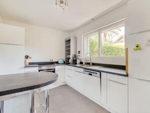 A modern kitchen with white cabinets, a black countertop, and a window providing natural light. - Les Nanous by Interhome (Saint-Raphaël)