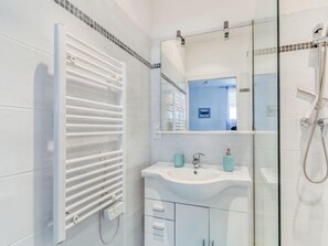 Un baño moderno con cabina de ducha de vidrio, un lavabo blanco con dos botellas y un perchero para toallas.