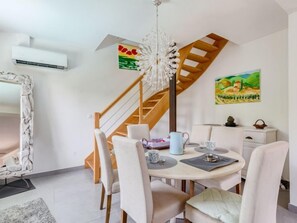 Un comedor con una mesa redonda, sillas, una araña, una escalera y obras de arte en las paredes.