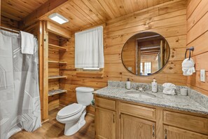Baño de cabaña de madera con inodoro, lavabo, espejo y perchero para toallas.