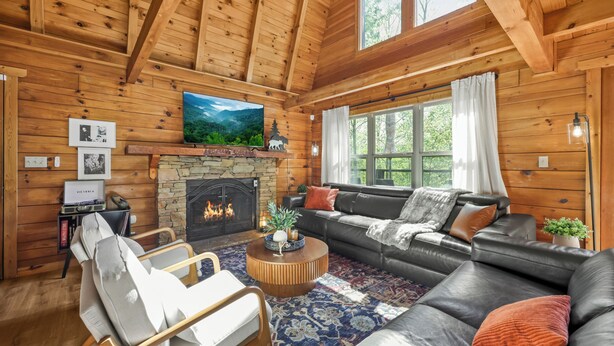 Ein Holzblockhaus-Innenraum mit Kamin, Ledersofa und einem an der Wand befestigten Fernseher.