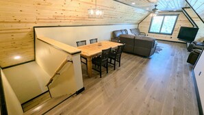 L’intérieur chaleureux d’un chalet avec une table à manger en bois, des chaises, un canapé et un téléviseur.