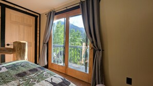Une chambre avec une grande fenêtre, une porte en bois et un lit recouvert d’une couvre-lit à motifs.