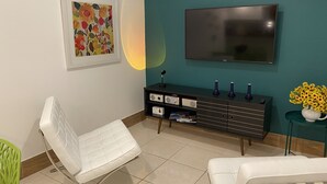 Una sala moderna con una mecedora blanca, un mueble de entretenimiento negro, un televisor de pantalla plana y un jarrón con girasoles.