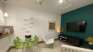 Un salón moderno con una mesa de comedor de cristal, sillas verdes, un sofá blanco, una pared de acento color turquesa, un televisor de pantalla plana y un radiador.
