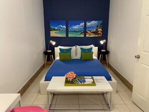 A hotel room with a bed, two bedside tables with lamps, a small white table with a vase and a book, and three framed pictures on the wall. - La Casita. (Tampa)