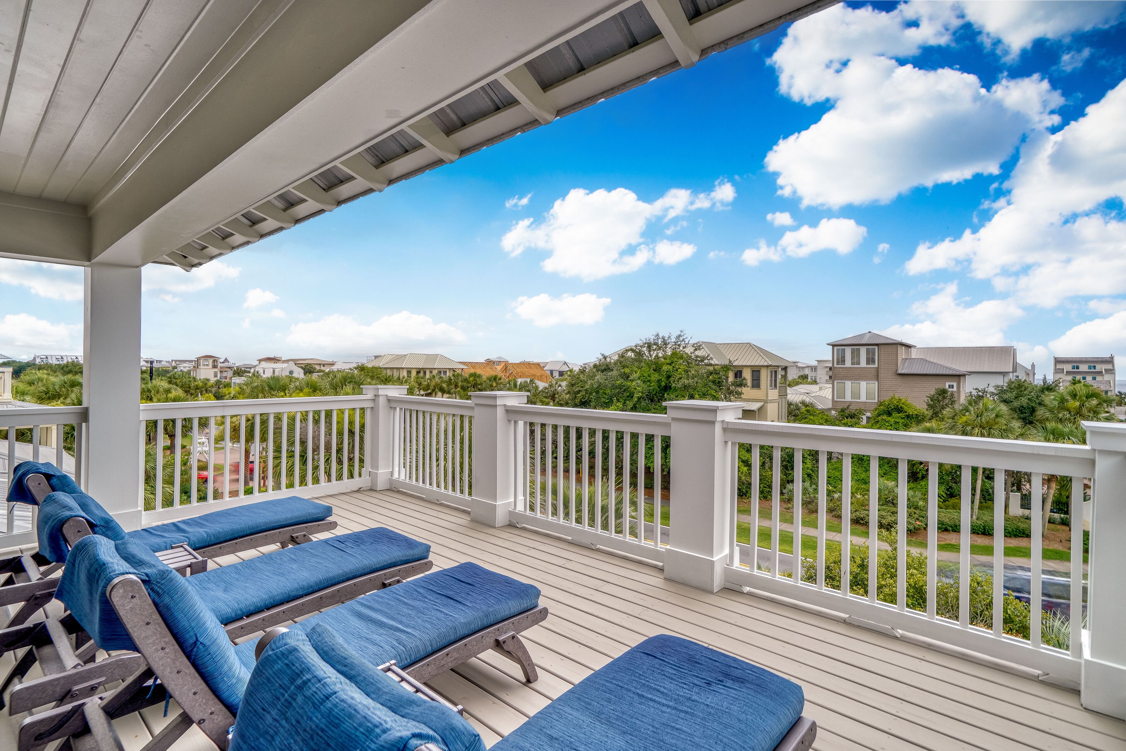 A covered outdoor area with lounge chairs and a white railing overlooking a residential neighborhood.