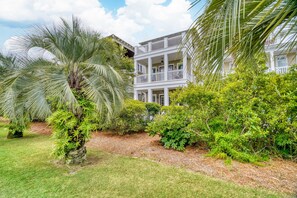 A two-story building with a balcony on the second floor, surrounded by lush greenery and palm trees.