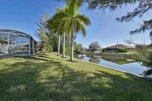 A house with a glass greenhouse, a small pond, and palm trees.