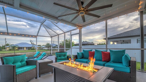 Eine überdachte Terrasse im Freien mit Feuerstelle, Korbmöbeln und Deckenventilator.
