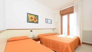 Habitación de hotel con dos camas, una ventana con cortinas, un radiador y un cuadro en la pared.