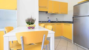 Una cocina compacta con armarios amarillos, un refrigerador de acero inoxidable y una mesa de comedor blanca con sillas amarillas.