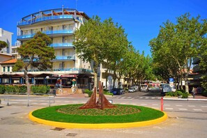 A multi-story building with a restaurant on the ground floor, a parking sign, and a central circular area with a tree and grass.