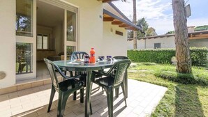 An outdoor patio with a table and chairs, a bottle, and a glass door leading to a covered area. - Holiday apartment with terrace (Lignano)