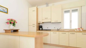 A modern kitchen with light-colored cabinets, a wooden countertop, a coffee maker, and a vase with flowers. - Holiday apartment with terrace (Lignano)
