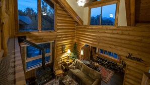 L’intérieur chaleureux d’un chalet en bois, avec une cheminée, des murs en bois et de grandes fenêtres offrant une vue sur le paysage extérieur.