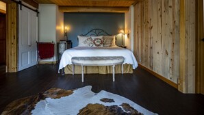 Une chambre avec un plafond en bois, un lit recouvert d’une courtepointe blanche, deux lampes de chevet, une table de chevet avec une lampe et un tapis en peau de vache sur le sol.