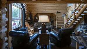 L’intérieur d’une cabane en rondins, avec une cheminée, des canapés en cuir, une table à manger et un escalier.