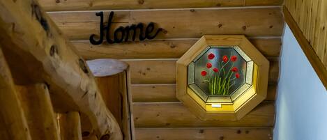Een houten trap met een 'Home' bord erboven, een zeshoekig raam met rode bloemen, en een kleurrijke muur met een patroon aan de onderkant.