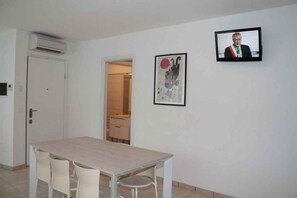 Een kamer met een eettafel en stoelen, een aan de muur bevestigde televisie en een deur die naar een andere kamer leidt.