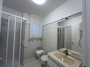 Een badkamer met een douchecabine van glas, toilet, wastafel met spiegel en raam met witte gordijnen.