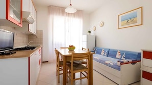 A compact living space with a kitchenette, dining area, and a sofa bed with a nautical theme. - Holiday apartment with air conditioning (Lignano)