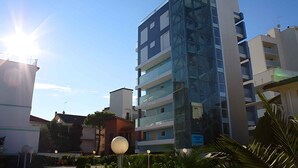 Un immeuble à plusieurs étages doté d’une façade moderne en verre, entouré d’autres bâtiments et de verdure.