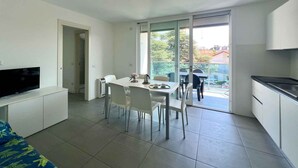A modern apartment with a dining area, kitchen, and a TV on a cabinet. - Holiday apartment with balcony, air conditioning and internet (Lignano)