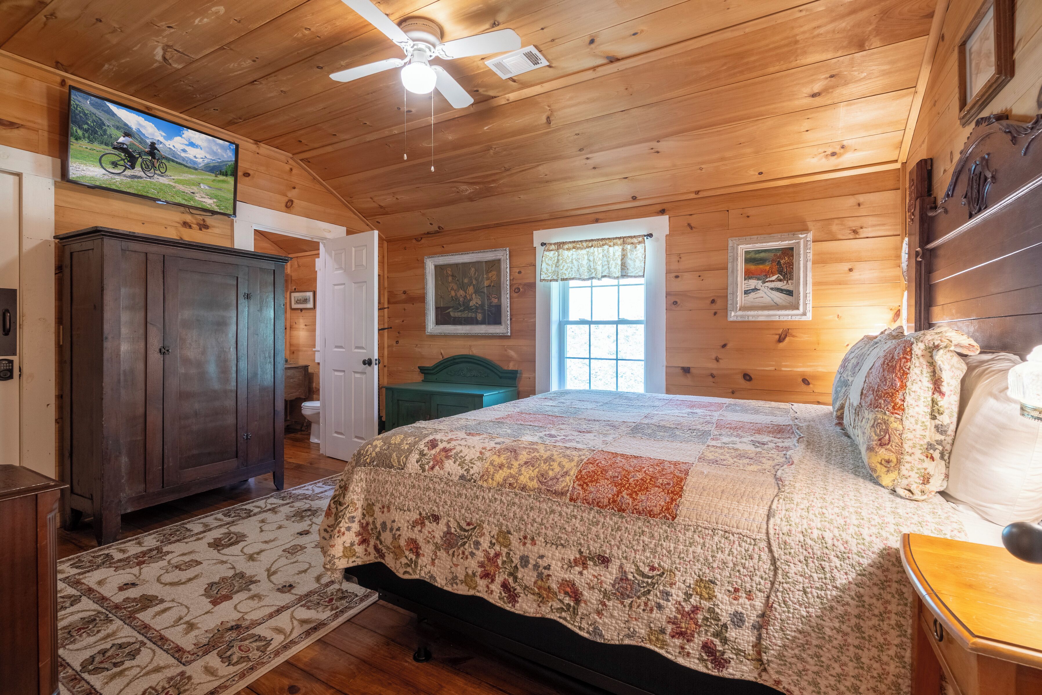 Une chambre dans un chalet en bois, avec un lit, un ventilateur de plafond, une télévision et une fenêtre.