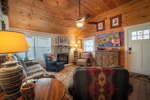 A cozy living room with a fireplace, wooden ceiling, and a television mounted on the wall. - Georgia Bell's| Vintage Farmhouse by Chattahoochee (Helen)
