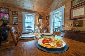 A wooden dining room with a table set for a meal, framed pictures on the walls, and a bear statue. - Georgia Bell's| Vintage Farmhouse by Chattahoochee (Helen)