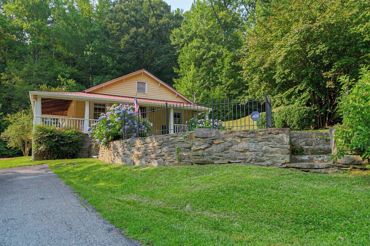 A two-story house with a porch, stone wall, and a flag.
